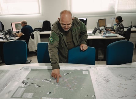 Nilton Luís Godoy Tubino leans over a desk, pointing at a large map, with colleagues working behind him
