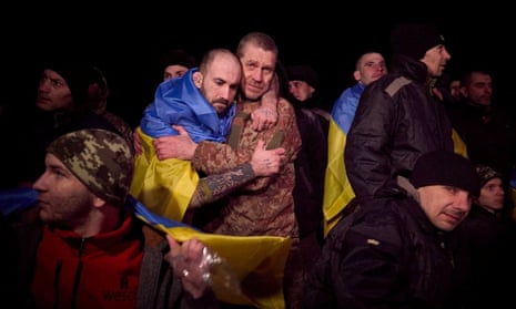 Two Ukrainian prisoners of war embrace each other in a crowd of PoWs, some wrapped in the Ukrainian flag