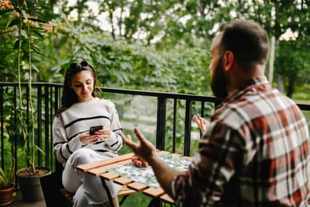 A man gestures with his hands talking while a woman looks at her moble phone.