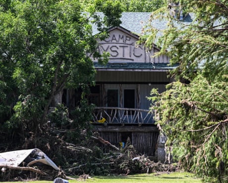 A building with 'Camp Mystic' written just under its roof visible through a gap in trees.