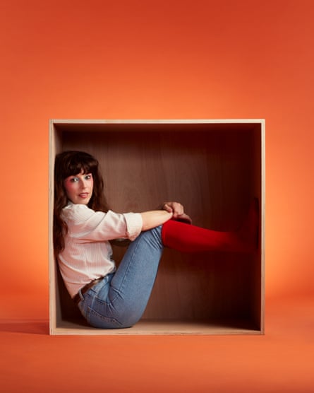 Bridget Christie photographed earlier this month. She is in a box, dressed as Kate Bush wearing a cream shirt, jeans with red knee-length socks over the top