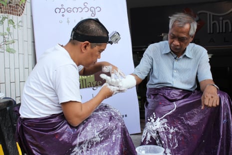 A south-east Asian man making a plaster cast of the hand of an older south-east Asian man