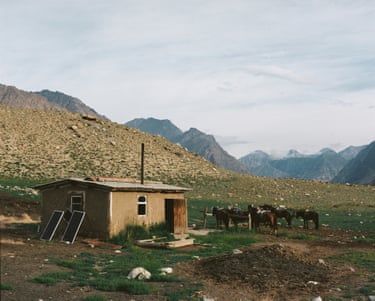 a squat living hut stands in wide empty landscape in Sary-Chat Nature Reserve, with horses grazing nearby Kyrgyzstan, 2023