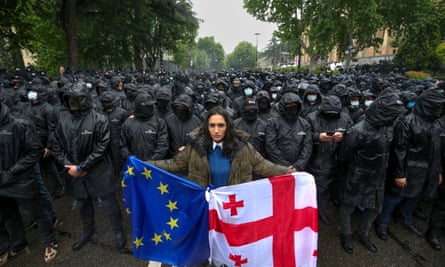 Demonstrator holds the Georgian and EU flags in front of police blocking a street