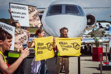 Activists hold banners, one of which reads ‘ban private jets’ in front of a plane