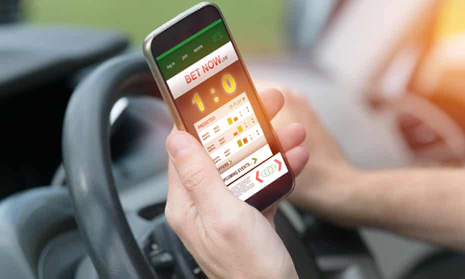 Hands at steering wheel hold phone showing betting app