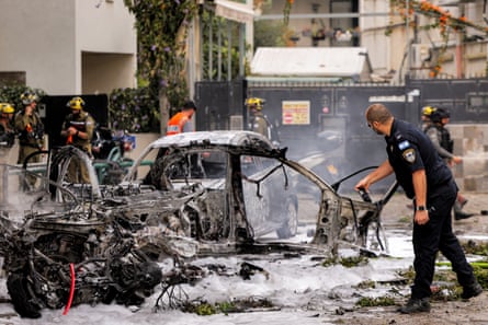 A police officer looks at a burnt-out car covered in extinguisher foam