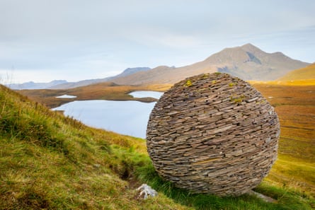 Huge ball built of stone and rocks on a hillside above a lake with mountains in the distance