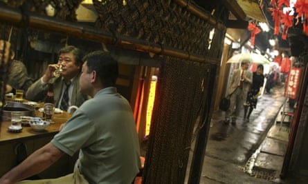 Two men in Tokyo sit drinking at a bar in an alleyway