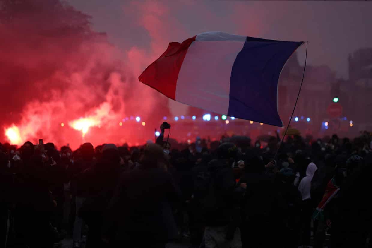A crowd waves a large French flag amid red smoke and flares during a Paris protest