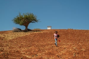 A girl runs across a field after taking water to the animals in a stable at Santa Catarina Estancia.