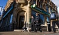 A man and a woman walking a dog walk past a branch of Lloyds on a street corner