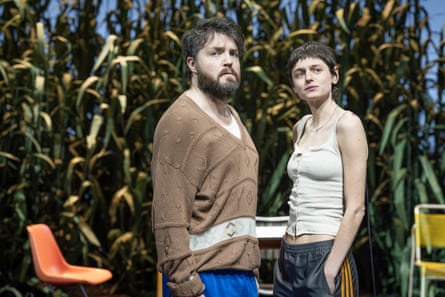 Tom Burke as Trigorin and Emma Corrin as Nina stand against a backdrop of high foliage in The Seagull.