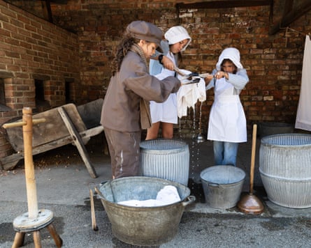 Three children in Victorian dress wash clothes in metal tubs