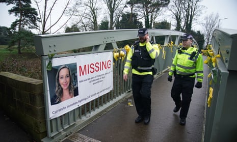 Police officers walk past a missing person appeal poster for Nicola Bulley and yellow ribbons and messages of hope tied to a bridge over the River Wyre