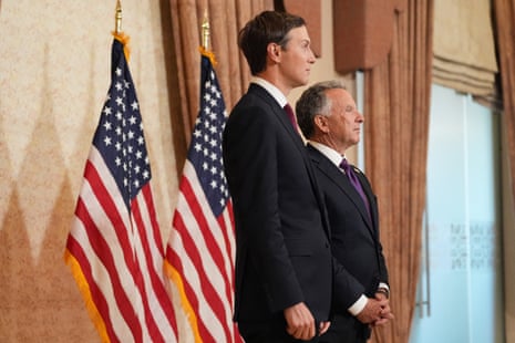 Two men in suits stand in front of two US flags.