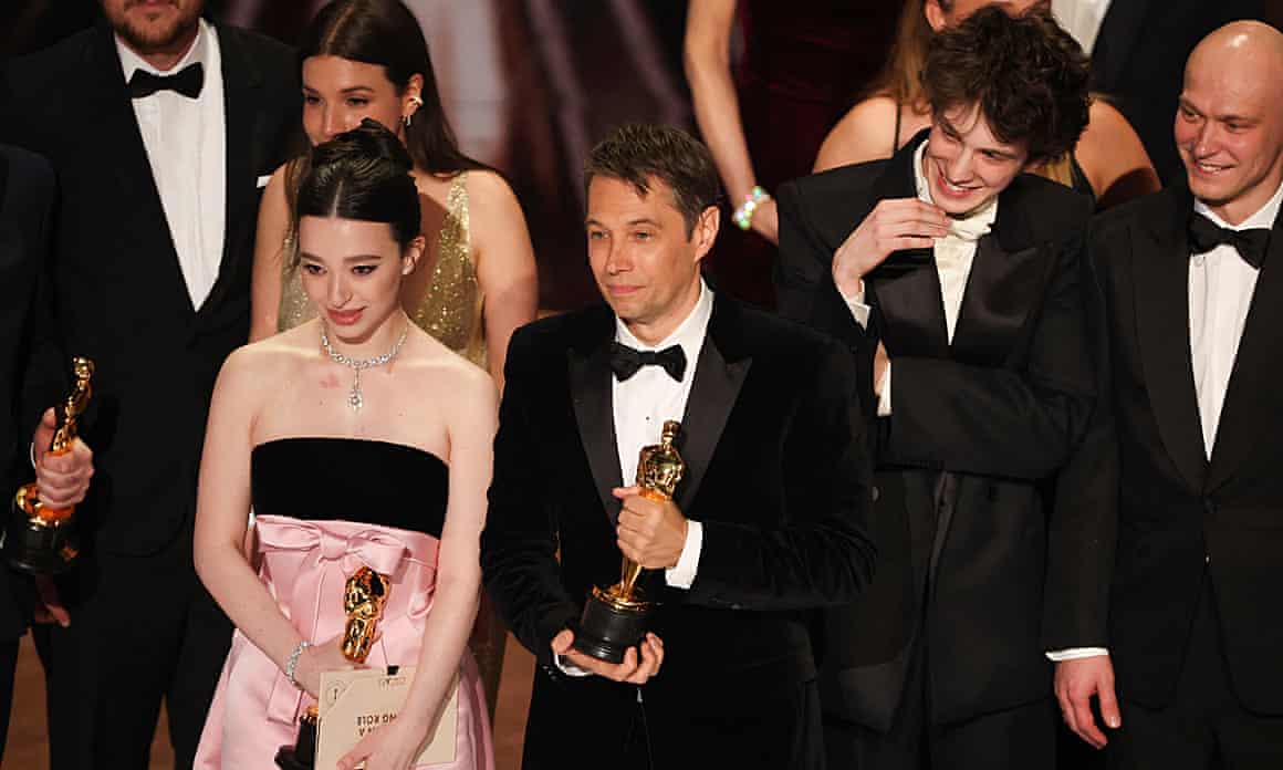 People in dresses or tuxedos stand on stage while clutching golden Oscar statuettes