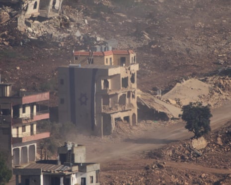 An Israeli flag covers a part of a damaged building in southern Lebanon, as seen from northern Israel, on Thursday