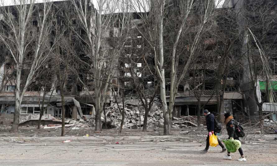 People walk past a destroyed apartment building in Mariupol.