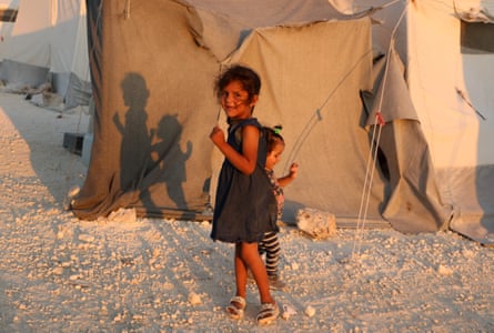 Two Syrian girls stand next to a tent at a camp for displaced people in the country’s northern Idlib province