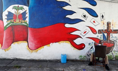 A man sits next to a mural in the Little Haiti neighborhood of Miami.