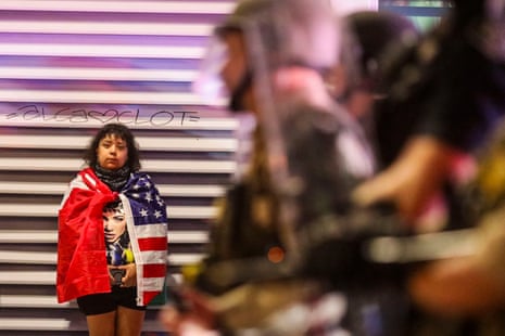 A demonstrator wrapped in an American flag stands on the side of a police line during the protests overnight.
