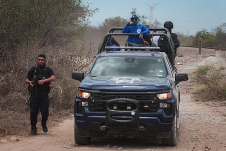 Women ride in the rear of a truck that is accompanied by uniformed and armed men.
