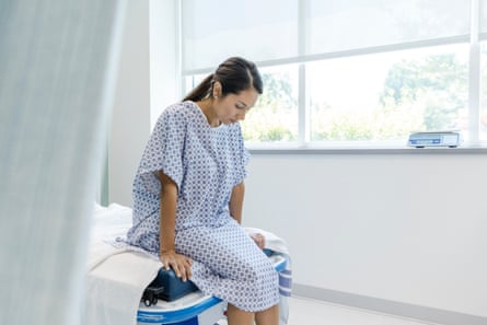 A woman in a hospital gown looks down to the floor