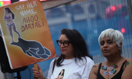 Two women, one with the slogan #mybody painted on her upper chest, the other with a placard of a woman in her underwear and the slogan 'say her name – Ahoo Daryaei'