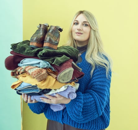 Woman wearing a blue knitted jumper and blond hair holds a pile of clothing in front of her