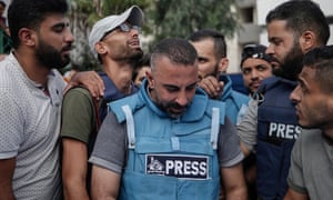 A man wearing a press jacket surrounded by other grieving men