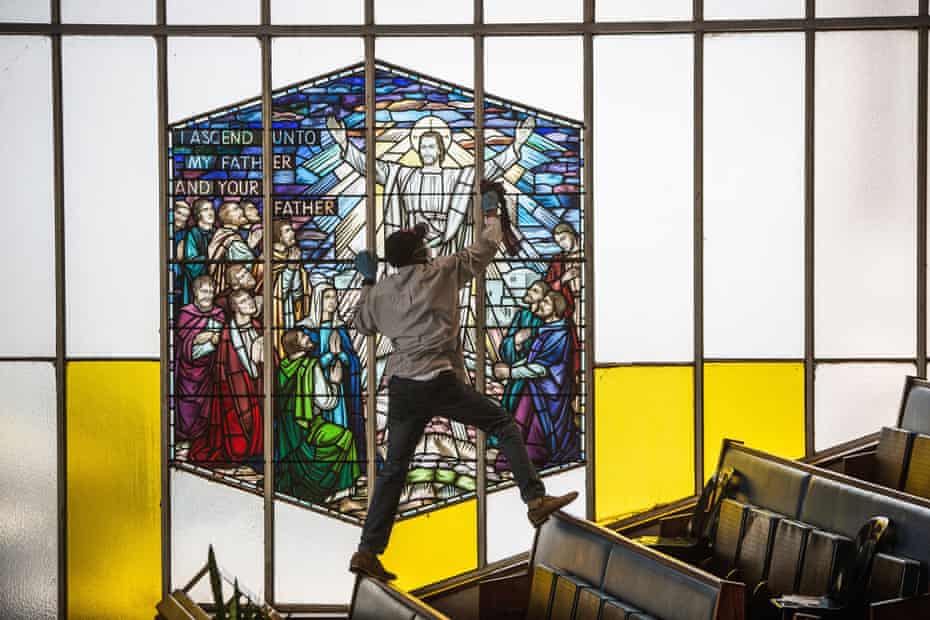 A man balances on top of the church pews to polish a stained glass wind