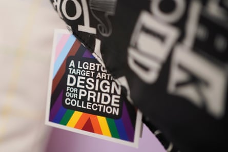 A label on maybe a bag is square and has both the trans and inclusive Pride flag on it: light pink, light blue, brown, black, purple, dark blue, gree, yellow, orange, and red.