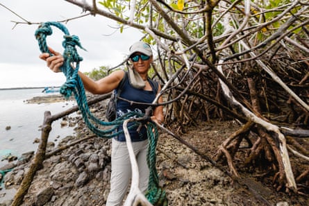 A woman removes fishing rope from a mangrove root at the shoreline