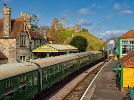 A steam locomotive departs Corfe station with the castle on a hill behind