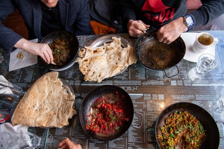 An overhead shot of four bowls of curry with people eating from them, using naan bread in place of forks