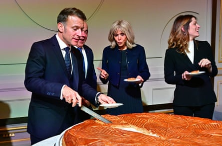 Emmanuel Macron serving himself a slice of a large epiphany galette pastry.