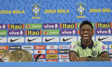 A cat (left) visits Brazil’s media conference before their World Cup defeat by Croatia, much to the amusement of the forward Vinícius Junior.
