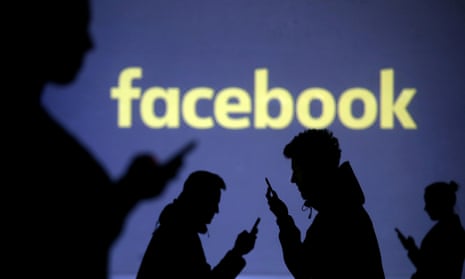 Silhouettes of mobile phone users are seen next to a screen projection of the Facebook logo
