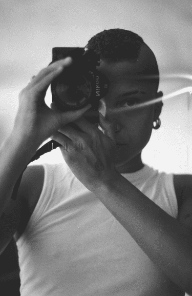 Black and white self-portrait photograph of Rene Matić holding a camera to their face