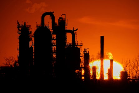 An oil refinery is silhouetted against the sky at sunset