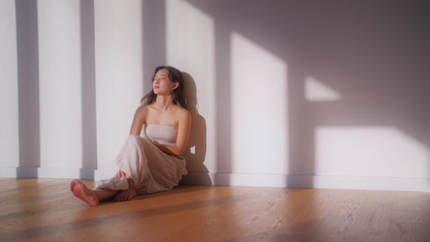 A portrait of a beautiful Asian woman sitting on the floor in front of a wall under the sunlight