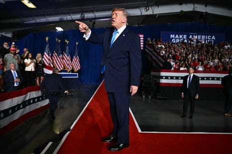 Donald Trump points to the crowd while speaking on a red carpet at a rally