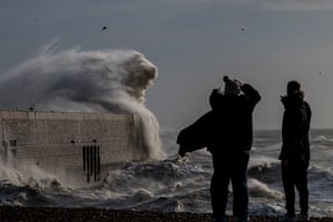 People look on as waves crash over a harbour wall 