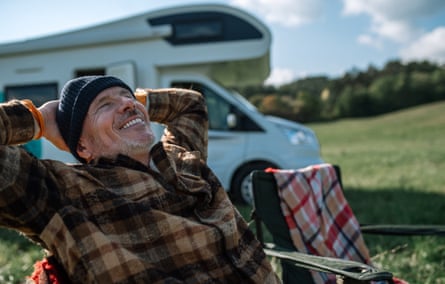 Senior man camping with caravan in nature.Happy senior man sitting and camping in front of camper.