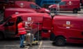 A postal worker pushes a crate towards some Royal Mail vans