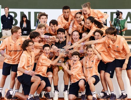 Carlos Alcaraz celebrates with the French Open men’s singles trophy alongside a number of ball girls and boys.