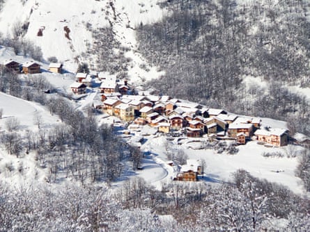 Overhead shot of a snow-laden village in a valley with wintry trees on the slopes either side