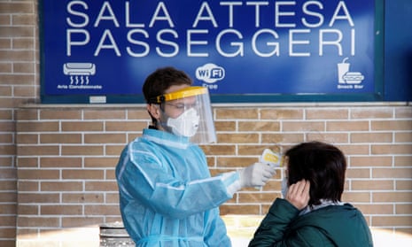 A medical worker checks the temperature of a passenger on arrival at a ferry port in the Sicilian city of Messina.