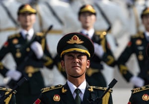 A close-up of a soldier in ceremonial uniform grimacing as he marches with others marching out of focus behind him
